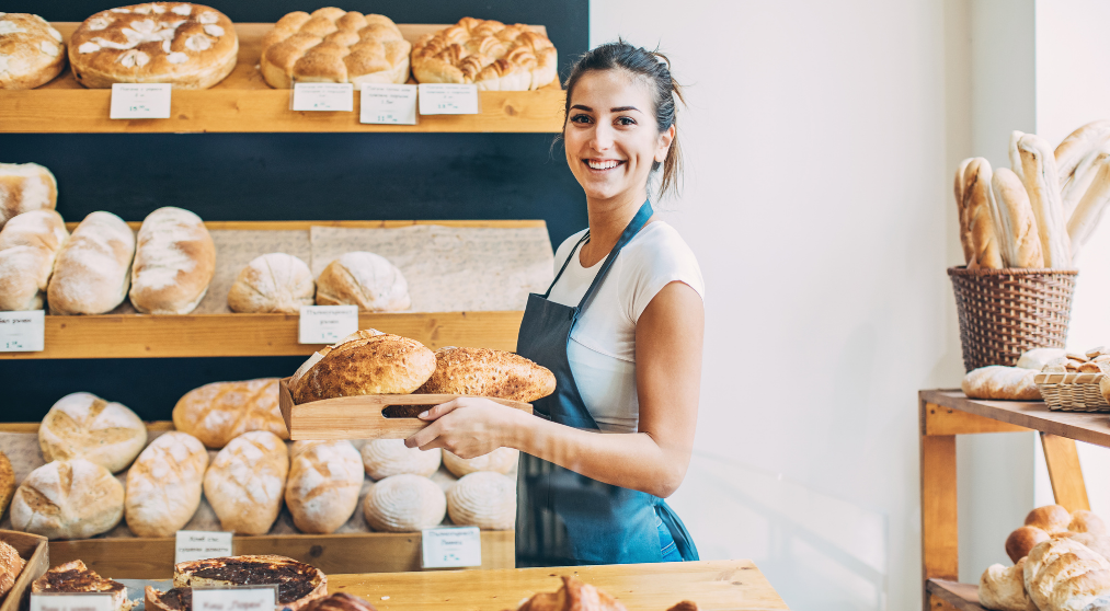 female-baker-standing-in-her-bakery-with-loaves-of-bread-in-hand