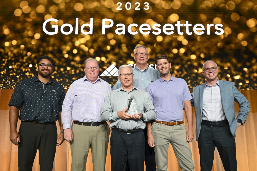 The Elevations wealth management team accepts their 2023 Gold Pacesetter award while posing against a gold background.